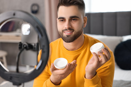 Beauty blogger reviewing cosmetic product and recording video with smartphone and ring lamp at homeの写真素材