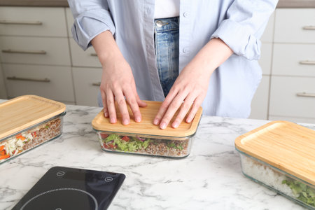 Healthy food. Woman closing glass container with meal at white marble table, closeupの写真素材