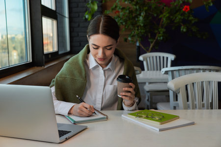 Young female student with laptop and coffee studying at table in cafeの写真素材