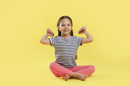 Cute little girl with dumbbells on yellow backgroundの写真素材