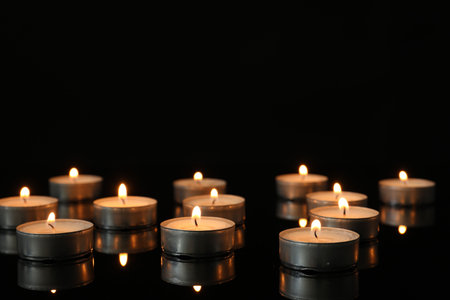 Many burning tealight candles on mirror surface against black backgroundの写真素材