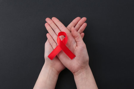 Woman with red awareness ribbon on black background, top view