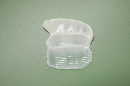 Face cream on green background, top view