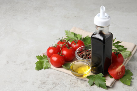 Bottle of balsamic vinegar, tomatoes, parsley and peppercorns on light gray table, space for text