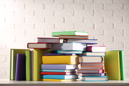 Stacks of many colorful books on white wooden table against brick wallの写真素材