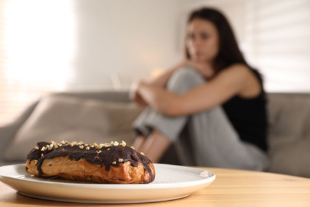 Eating disorder. Woman sitting on sofa indoors, focus on eclairの写真素材