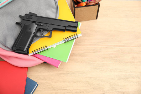 School stationery, gun and backpack on wooden desk, above view. Space for textの写真素材