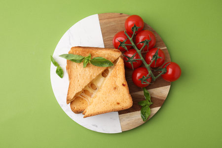 Pieces of toasted bread with melted cheese, tomatoes and basil on green background, top viewの写真素材