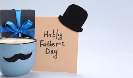 Greeting card with phrase Happy Father's Day, gift and cup of coffee on light background, space for textの写真素材