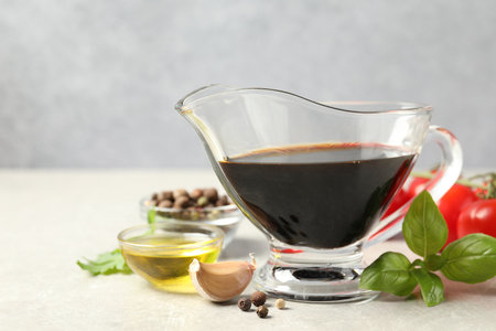 Balsamic vinegar in gravy boat, oil, basil and spices on gray textured table, space for textの写真素材