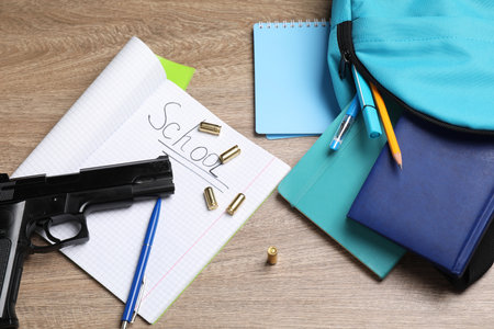 Gun, bullets and school stationery on wooden table, flat lay