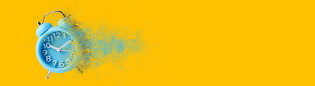Light blue alarm clock dissolving on orange background, banner design with space for text. Flow of timeの写真素材