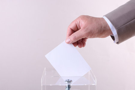 Man putting his vote into ballot box against light gray background, closeupの写真素材