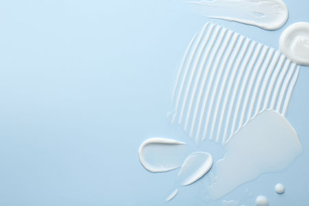 Samples of face cream on light blue background, top view. Space for textの写真素材