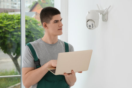 Technician with laptop installing CCTV camera on wall indoorsの写真素材