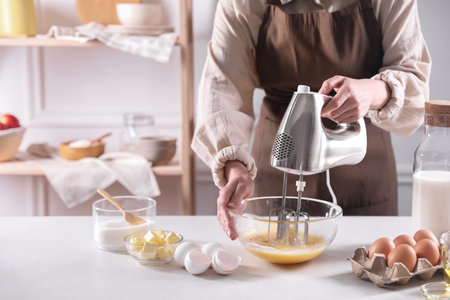 Woman making dough with mixer in bowl at table, closeup