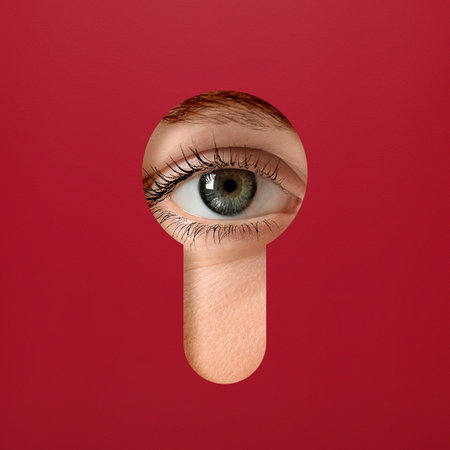 Woman looking through keyhole in red surfaceの写真素材