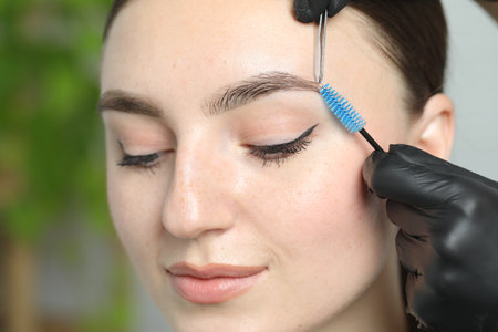 Beautician making eyebrow correction to young woman in beauty salon, closeup