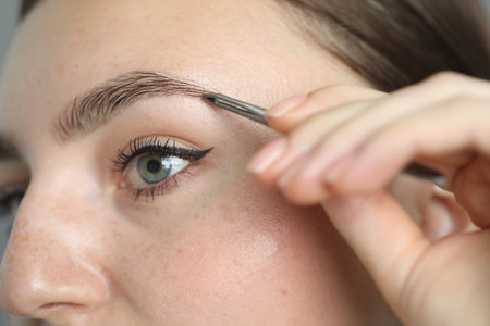 Young woman plucking eyebrow with tweezers, closeup
