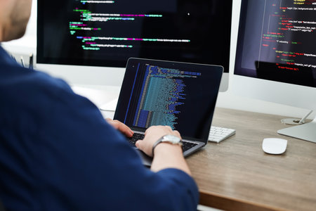 Programmer working with laptop at desk in office, closeup