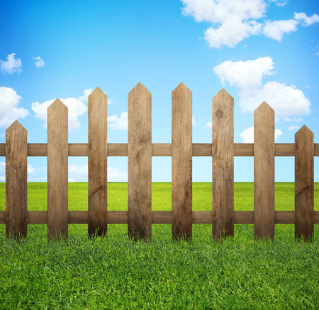 Wooden fence and green grass under blue sky with clouds outdoorsの写真素材