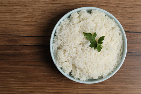 Tasty cooked rice with parsley in bowl on wooden table, top view. Space for textの写真素材