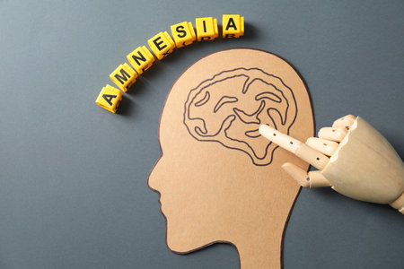 Yellow cubes with the word Amnesia and mannequin hand pointing at drawing of brain on gray...