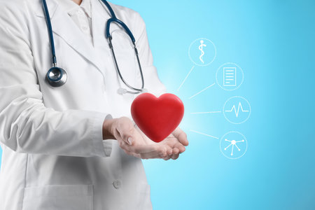 Doctor holding red heart on light blue background, closeup. Icons near handsの写真素材