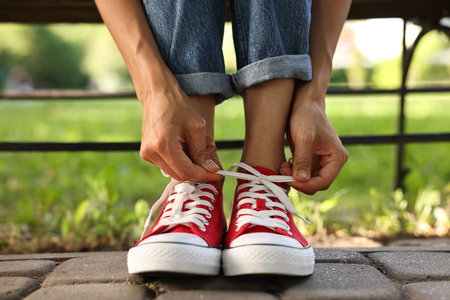 Woman tying shoelace of red sneaker outdoors, closeupの写真素材