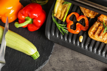 Electric grill with tasty meat, spices and vegetables on gray textured tableの写真素材