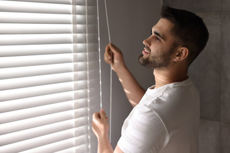 Man adjusting window blinds at home, space for textの写真素材