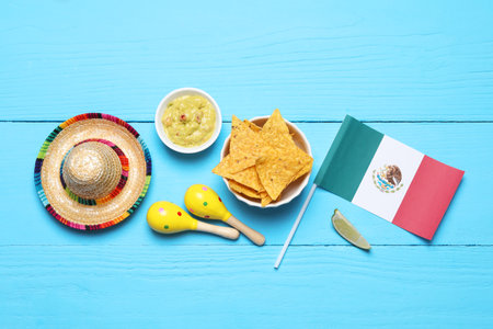 Mexican flag, sombrero hat, maracas, nachos chips and guacamole on light blue wooden table, flat layの写真素材