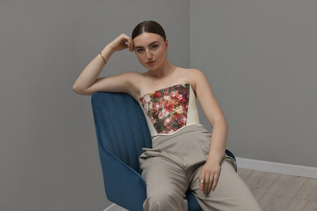 Beautiful young woman in stylish corset on armchair indoorsの写真素材