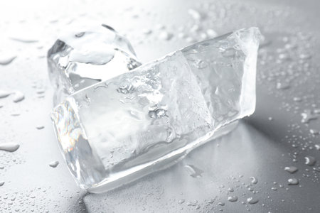 Pieces of clear ice and water drops on light grey table