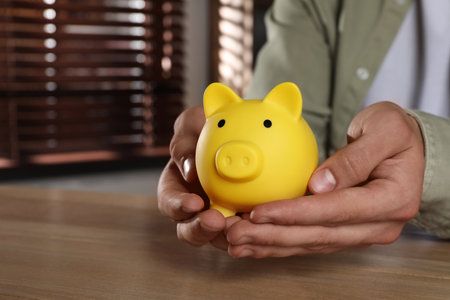 Man with yellow piggy bank on wooden table, closeupの写真素材