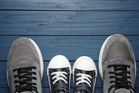 Big and small shoes on blue wooden table, top view. Space for text