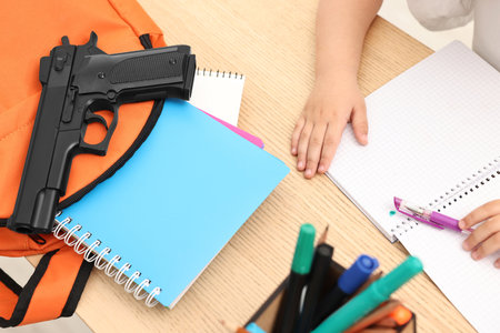 Child at desk with school stationery and gun, closeupの写真素材