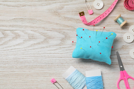 Light blue pincushion with pins and other sewing tools on wooden table, flat lay. Space for textの写真素材