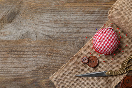 Checkered pincushion with pins and other sewing tools on wooden table, flat lay. Space for textの写真素材
