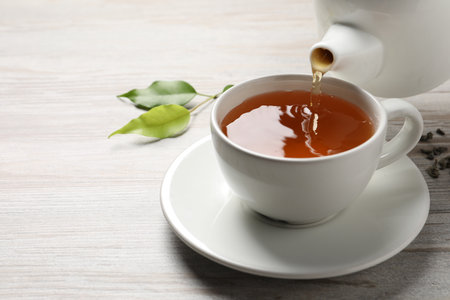Pouring refreshing green tea into cup at gray wooden table, closeup. Space for text