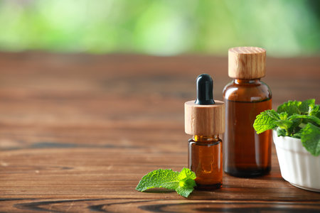 Bottles of mint essential oil and fresh leaves on wooden table, space for textの写真素材