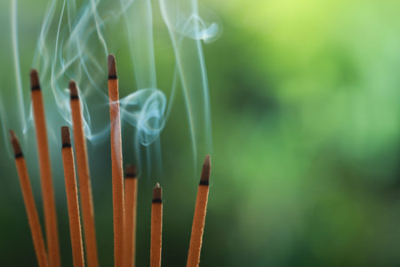 Incense sticks smoldering on green blurred background, space for textの写真素材