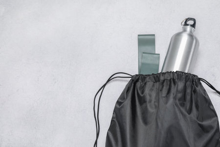 Black drawstring bag, thermo bottle and fitness elastic band on light background, top view. Space for textの写真素材