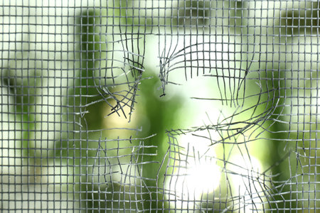 Torn window screen against blurred background, closeup
