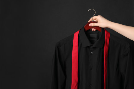 Woman holding hanger with shirt and necktie on black background, space for textの写真素材