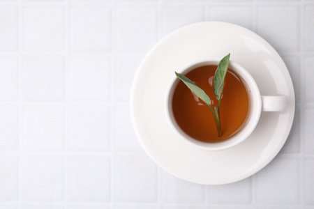 Aromatic herbal tea with sage in cup on white tiled table, top view. Space for textの写真素材