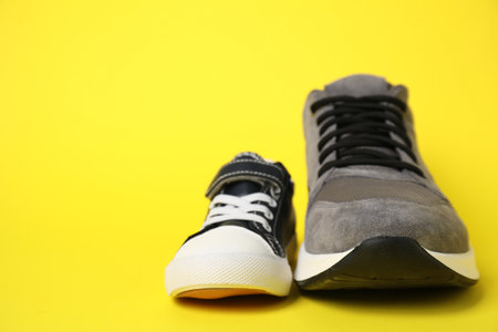 Big and small shoes on yellow background, space for textの写真素材