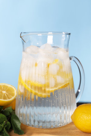 Freshly made lemonade with mint in jug on wooden table against light blue background
