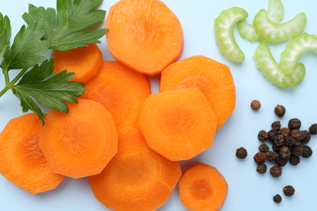 Slices of fresh ripe carrot, celery and spices on light blue background, flat layの写真素材