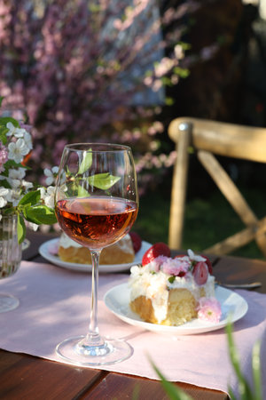 Vase with spring flowers, wine and cake on table served for romantic date in gardenの写真素材
